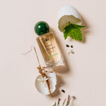 Jardin Mamzelle Perfume bottle with green cap and leaves on a beige background
