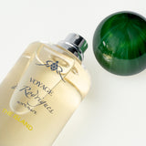 Perfume bottle labeled 'Voyage Rodrigues' with a green sphere on a light background