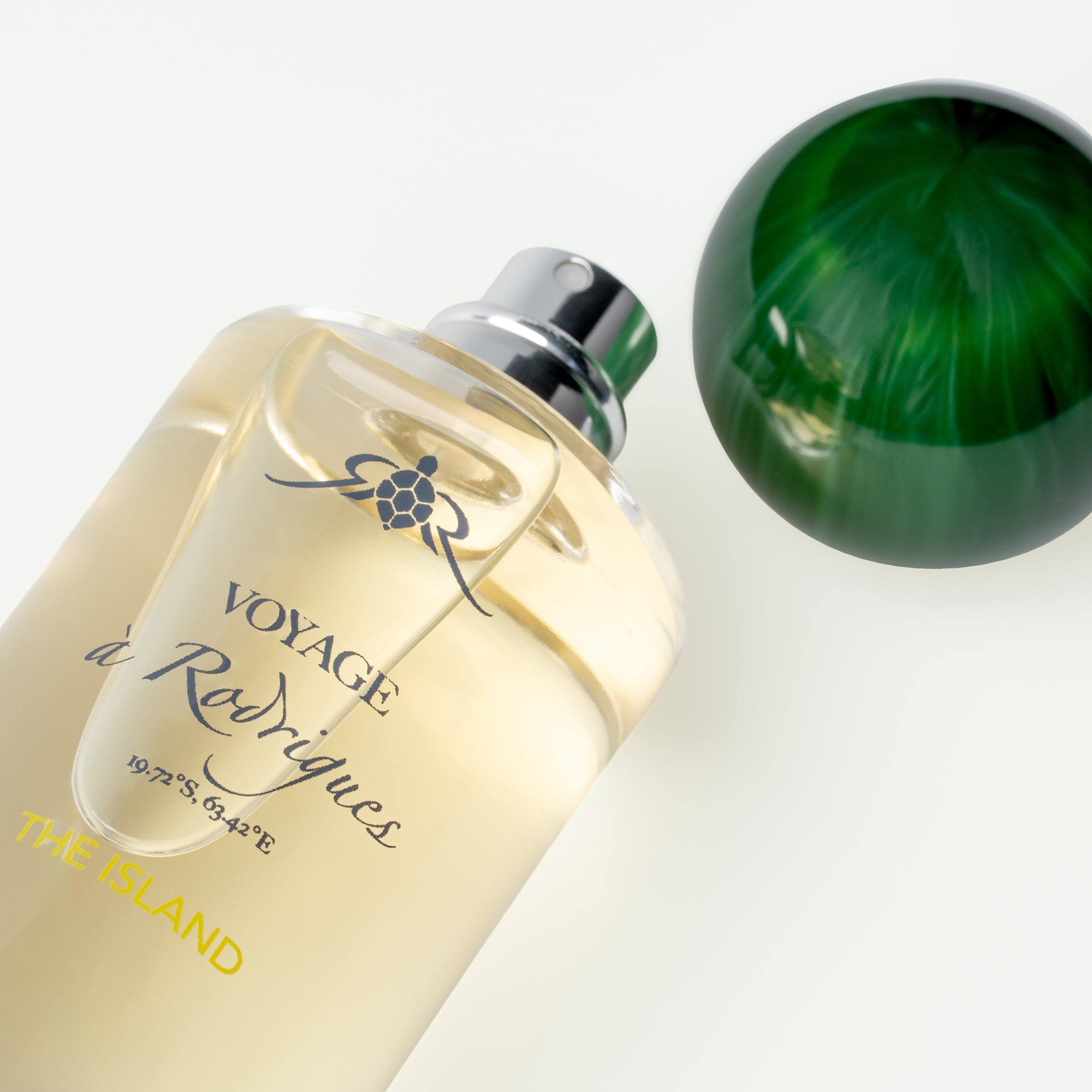 Perfume bottle labeled 'Voyage Rodrigues' with a green sphere on a light background